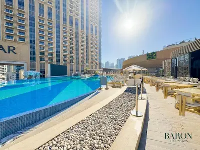 a hotel swimming pool with tables and benches and buildings at The Glamorous in Dubai