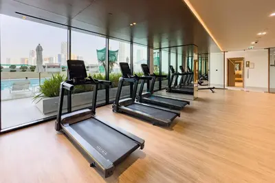 a row of treadmills in a gym with windows at Near Gadaf Community Park, Few Minutes Walk to Circle Mall, Short Drive to Dubai Miracle Garden and Butterfly Garden - Binghatti Amber, JVC by Deluxe Holiday Homes in Dubai