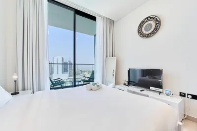 a white bedroom with a large bed and a large window at FAM Living Stylish Studio Apartment in Binghatti Azure JVC in Dubai