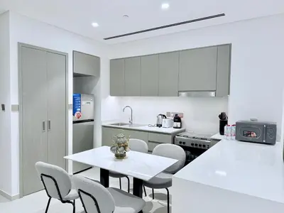 a white kitchen with a white table and chairs at Balcony Bliss 1BR with City View Pool & Gym in Dubai