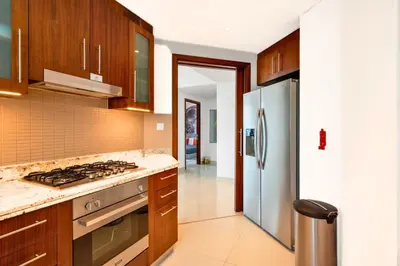 a kitchen with wooden cabinets and a stainless steel refrigerator at Cosmic Address 2BR Burj Views above Dubai Mall - By Maxx Value Homes in Dubai
