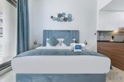 a bedroom with a large white bed and a kitchen at Cozy Studio in Orchid - Damac Hills Dubai in Dubai