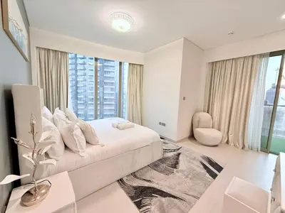 a white bedroom with a bed and a large window at Skyline Escape 2BR with Balcony Pool & Gym in Dubai