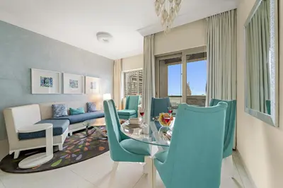 a living room with a glass table and blue chairs at FIRST CLASS 1BR Iconic Burj Khalifa View in Dubai