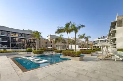 a swimming pool in a resort with palm trees and buildings at Chic Studio in Vibrant Oxford Residence in Dubai