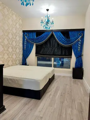 a bedroom with a bed with blue curtains and a chandelier at JLT Luxury New 2BHK in Dubai