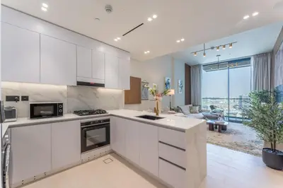 a kitchen with white cabinets and a living room at Cozy Apartment Gym and Pool Heart of JVC in Dubai