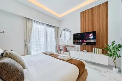 a white bedroom with a large bed and a tv at Modern & Elegant Studio Apartment in Azizi Riviera in Dubai