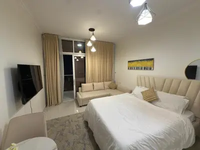 a bedroom with a bed and a couch and a television at Carson Tower- A Damac Hills 1, Studio Apartment in Dubai