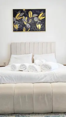 a bed with white sheets and a picture on the wall at Modern Apartment in Regina Tower JVC - Easy Access to JBR, Circle Mall & Dubai Hills Mall in Dubai