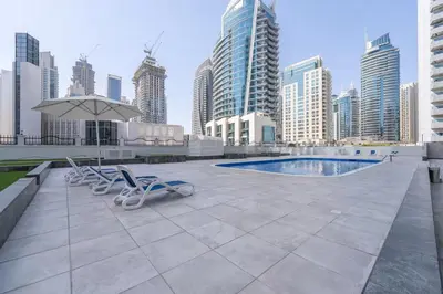 a pool with two chairs and an umbrella and buildings at Vogue Marina Diamond Near JBR Beach and Marina Mall, One Bedroom Apartment with Balcony and City View, Access to all Amenities, Walkable to Sobha Realty Metro Station and Bus Stop in Dubai