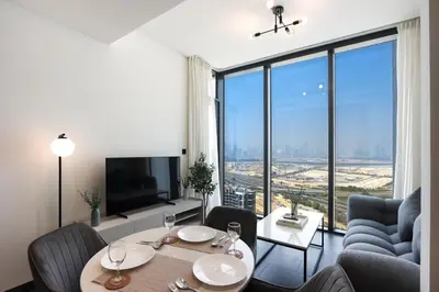 a living room with a table and chairs and a large window at Stylish 1BR with Skyline Views Sobha Crest, Hartland in Dubai