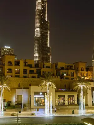 a tall building with palm trees in front of it at night at Premium1BR Retreat with Burj Khalifa View in Dubai