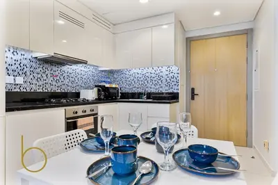 a kitchen with a table with plates and wine glasses at Bookable 2 bed Damac Aykon City with Balcony & Pool access in Dubai
