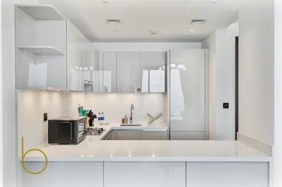 a white kitchen with a sink and a microwave at Bookable 2 Bed Crest Sobha Hartland with Burj view in Dubai