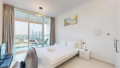 a white bedroom with a bed and a large window at Vacationer I Luxury Studio I Scenic Golf Course & Skyline Views I Carson B Tower in Dubai Marina