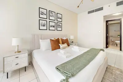a white bedroom with a large bed and a night stand at Silkhaus Luxurious 1BR at Sky Gardens in DIFC in Dubai