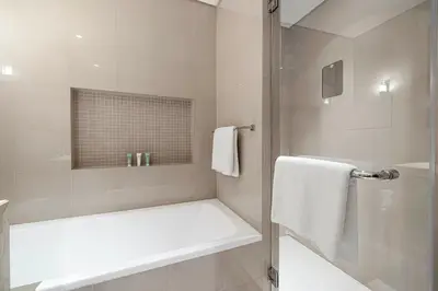a white bathroom with a tub and a shower at Skyline Aura 1 & 2 Bedroom Apartments I Burj Khalifa & Fountain Views I Dubai Mall Access I Parking, Gym, Wi-Fi & Infinity Pool in Dubai