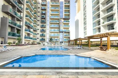 a swimming pool in front of a building at Balcony Overlooking the Community, Quick Metro Access,Short 15-Minute Drive to Ibn Battuta Mall, Viktoria Residency, Al Furjan by Deluxe Holiday Homes in Dubai