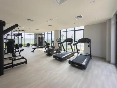 a gym with several treadmills and cardio machines at Studio Near Meydan Golf Club, 15-Minute Drive to Dubai Mall, Burj Khalifa and Downtown Attractions, Azizi Riviera 46, Al Merkadh by Deluxe Holiday Homes in Dubai