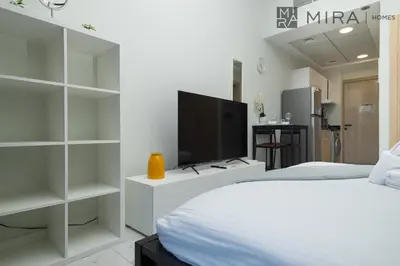 a white bedroom with a tv and a bed at Mira Holiday Homes - Luxury, Stylish & Cozy Studio in Downtown Jebel Ali in Dubai