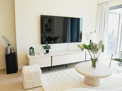 a white living room with a large tv on the wall at Stylish-2BR, Burj Royale, 3 min walk to Dubai Mall in Dubai