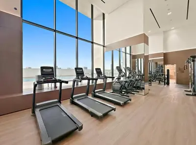 a gym with a row of treadmills and windows at High Rise Studio Pool Gym Binghatti Gardenia JVC in Dubai