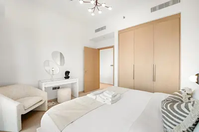 a white bedroom with a large bed and a chair at Spacious 1BR in Downtown with Balcony & Pool in Dubai