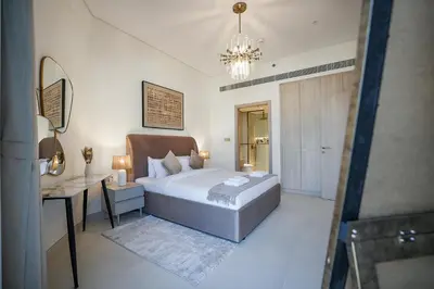 a bedroom with a bed and a desk and a chandelier at EasyGo - Modern 1BR with Balcony & Amenities in Arjan in Dubai