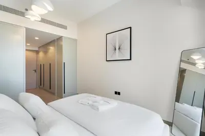 a white bedroom with a white bed and a mirror at Gala Guests - Golf Gate Residences with Panoramic Golf Views in Dubai