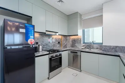 a kitchen with white cabinets and a black refrigerator at Gala Guests - Golf Gate Residences with Panoramic Golf Views in Dubai
