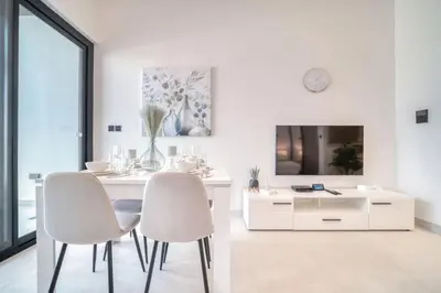 a white dining room with two chairs and a table at Bright Studio in Binghatti Canal in Dubai