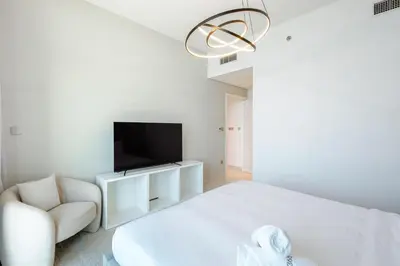 a bedroom with a white bed and a tv and a chair at Dubai Dream Stay - 2-BR with Sea View in Beach Vista in Dubai