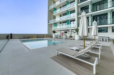 a pool with chairs and umbrellas next to a building at Studio Just Minutes Drive from Miracle Garden, Near Local Parks and Circle Mall, Binghatti Azure, JVC by Deluxe Holiday Homes in Dubai