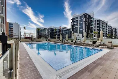 a large swimming pool with chairs and buildings at Cozy Studio 15 Min From Burj Khalifa in Dubai