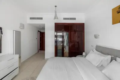 a white bedroom with a large bed and a dresser at Cozy 1BR with gym & pool in heart of Marina - Opal Tower in Dubai