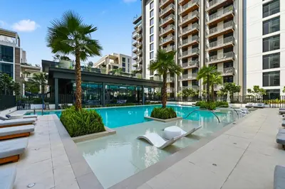 a swimming pool with lounge chairs and palm trees at New Cozy Studio, Ideal for 2 in Kensington Waters in Dubai