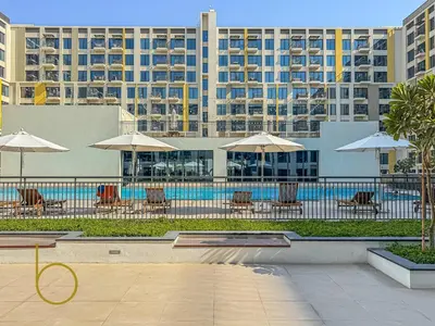 a pool with chairs and umbrellas in front of a building at Bookable 1 Bed Liva Tower with Pool & Garden in Dubai