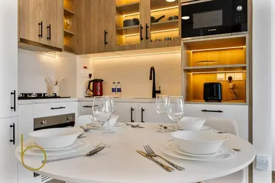 a kitchen with a white table with plates and wine glasses at Bookable 1 Bed Liva Tower with Pool & Garden in Dubai