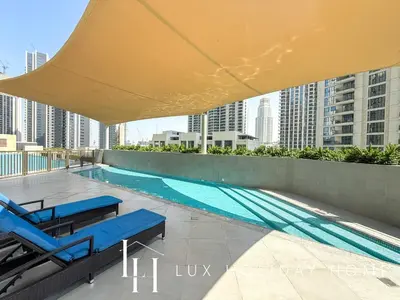 a swimming pool with blue chairs and a large umbrella at LUX The Creekside Skyline View Suite in Dubai