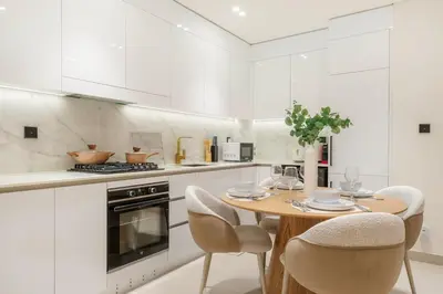a white kitchen with a wooden table and chairs at FIRST CLASS 1BR Luxurious JVC Blissful Escape in Dubai
