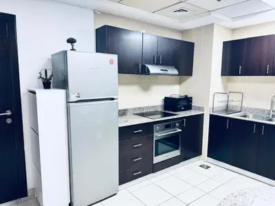a kitchen with a white refrigerator and black cabinets at COZY 1BD in Dubai Marina in Dubai