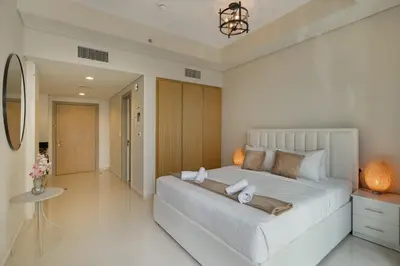 a white bedroom with a large white bed and a table at Aykon Tower - Studio Apartment - Allsopp & Allsopp in Dubai