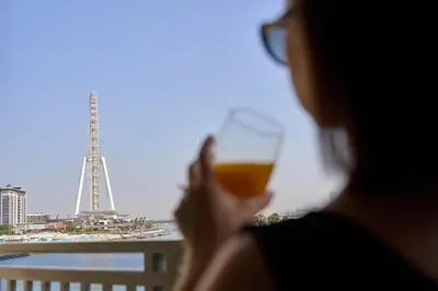 a woman holding a glass of wine looking at the eiffel tower at Coastal 1BR with Balcony and Marina Ain Dubai Bluewaters Views in Dubai
