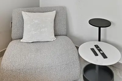 a gray chair with a remote control next to a table at Deluxe Studio for 2 in Peninsula One, Business Bay in Dubai
