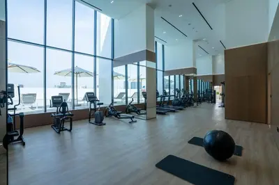 a gym with a lot of exercise equipment and windows at Warm Modern 2BR Retreat with Private Pool in JVC! in Dubai