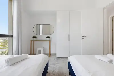 a white room with two beds and a mirror at Town Square Zahra 2B - 2 Bedroom Apartment - Allsopp & Allsopp in Dubai