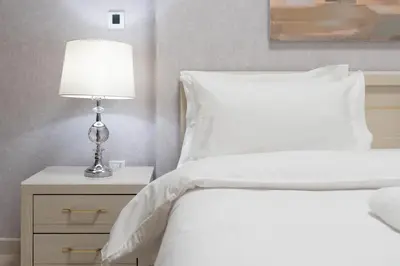 a bed with white sheets and a lamp on a night stand at Dubai Luxury 2BR - Pool, Gym & Burj Khalifa View in Dubai