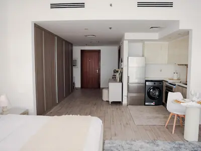 a bedroom with a white bed and a kitchen at Elegant Studio with Pool & Gym in JVC in Dubai