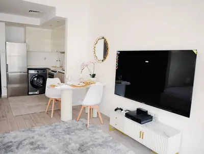 a living room with a white table and a large tv at Elegant Studio with Pool & Gym in JVC in Dubai